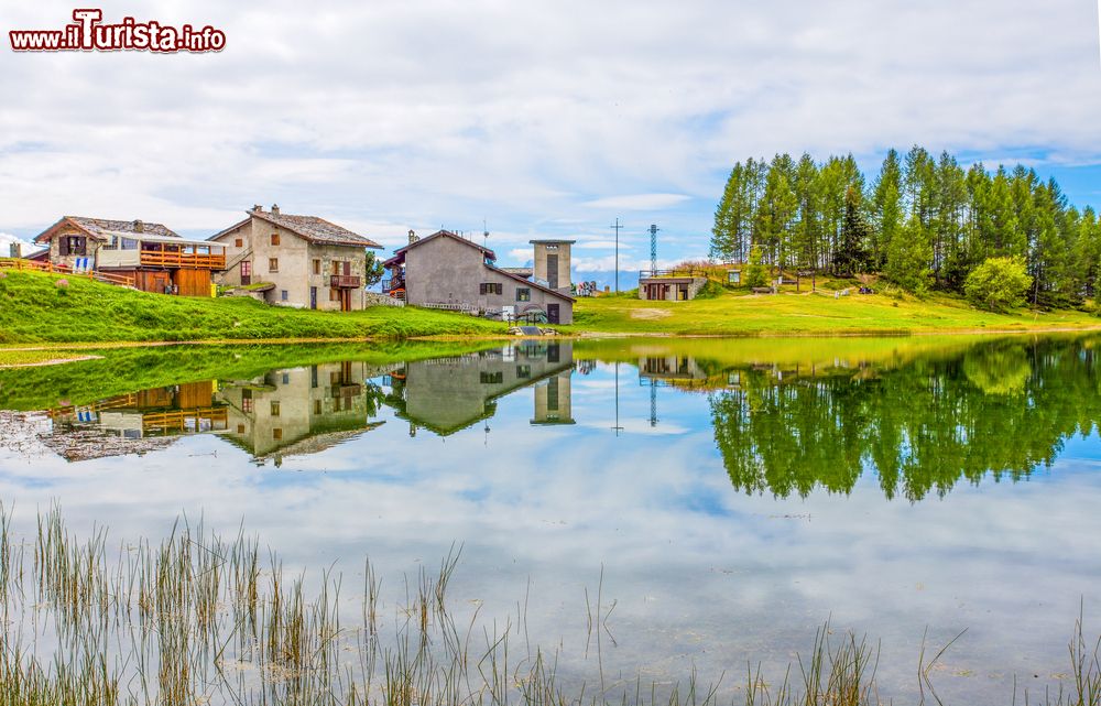 Immagine Case riflesse nel lago Lod nei pressi del villaggio di Chamois, Valle d'Aosta. Il lago si trova sotto il Monte Charvaz a 2019 metri di altitudine ed è raggiungibile con la seggiovia da Chamois nei periodi di apertura. Da qui si possono vedere le cime che circondano il paese, da quella di Longhede fino al Chateau des Dames.