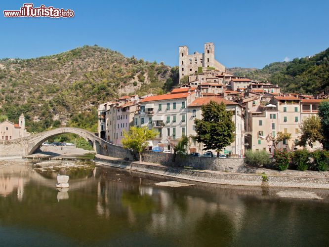 Immagine Panorama del villaggio medievale di Dolceacqua in Liguria, Italia - Una bella immagine del ponte romanico e del castello dei Doria riflessi nelle acque del fiume Nervia. La fortezza domina l'intero paese per il quale ha svolto un importante ruolo sociale. Oberto Doria, capostipite della dinastia, acquistò dai conti di Ventimiglia nel 1270 la torre circolare originaria; nel corso del '400 venne realizzato il baluardo difensivo verso est e le torri quadrangolari che dominano il borgo. Nel XVI° secolo Stefano Doria trasformò il castello in una lussuosa residenza © Maria Veras / Shutterstock.com