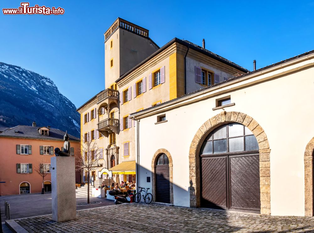 Immagine Centro storico di Briga, Svizzera: una statua con basamaneto in pietra e un antico edificio con torre.