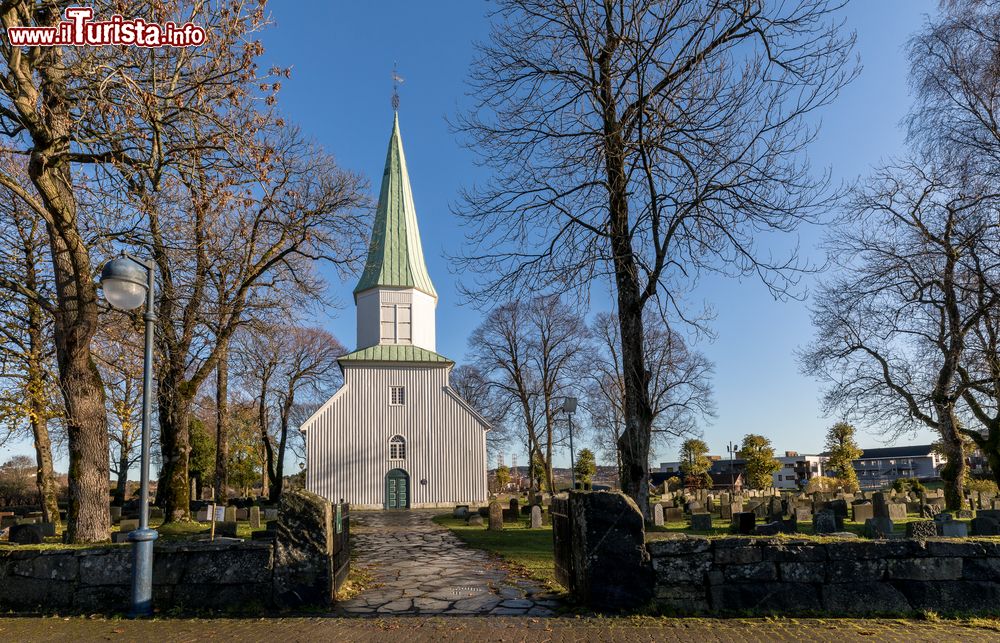 Immagine Chiesa bianca in legno con campanile a Kristiansand, Norvegia. A questo grazioso edificio religioso si accede tramite un vialetto in pietra affiancato dal cimitero.
