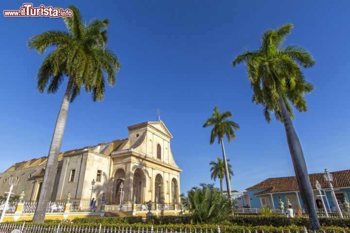 Immagine La Chiesa della Santissima Trinità all'ombra delle palme di Trinidad, Cuba - questa splendida chiesa, posizionata di fronte al parco di Plaza Major, ricopre una posizione di grande importanza sia a Trinidad sia, più in generale, a Cuba, in quanto è la chiesa più grande di tutta l'isola - © haraldmuc / Shutterstock.com