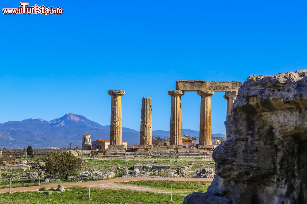 Immagine Colonne al Tempio di Apollo nell'antica Corinto, Grecia. Sullo sfondo, una chiesa e la sagoma delle montagne.