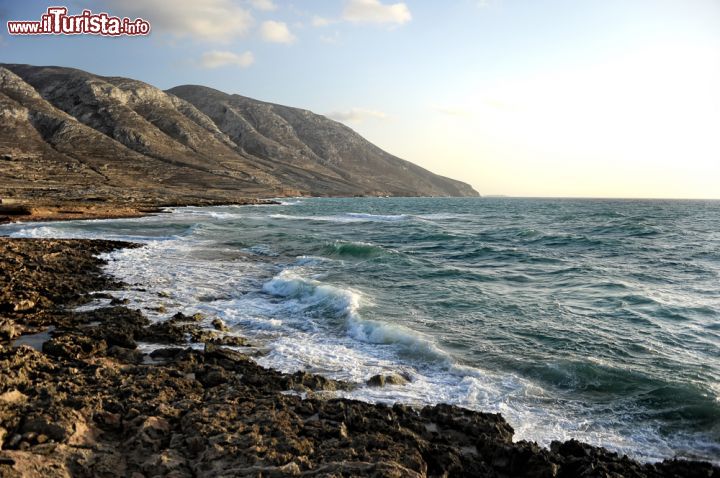 Immagine La vista generosa che regala la costa selvaggia dell'isola di Kassos, Dodecaneso (Grecia) - La natura per definizione rappresenta probabilmente la scenografia più bella presente nel grande gioco dell'umanità eppure, certe viste riescono a creare un ambiente più denso di altri, come in questo caso. Il gioco che riesce a fare il mare così calmo e placido a confronto della costa selvaggia così apparentemente primitiva e appassionata al tempo stesso, non può fare a meno di splendere in tutta la sua contraddizione. Quando poi il cielo si apre generosamente in un momento diurno così caldo, il risultato finale è unico - © Antlio / Shutterstock.com