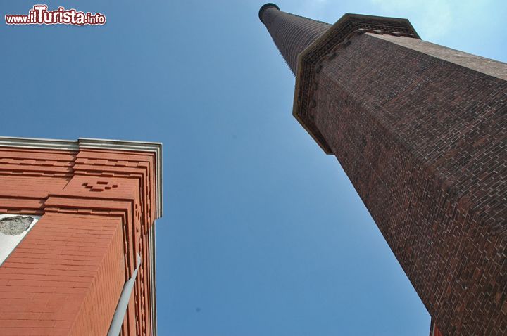 Immagine Dettaglio della ciminiera del Cotonificio Crespi - la ciminiera, alta ben 70 metri, fu costruita all'ingresso dell'edificio principale della fabbrica, allo scopo di disperdere i residui della combustione del carbone, utilizzato nei processi di lavorazione del cotone. Ai piedi di questa imponente struttura, una maestosa cancellata in ferro battuto in stile liberty. 