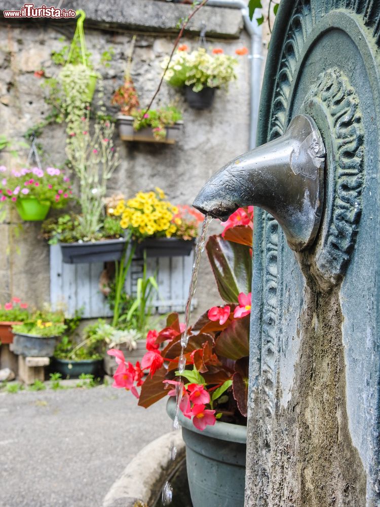 Immagine Dettaglio della fontana nel centro di Saint-Bertrand-de-Comminges (Francia). Sullo sfondo, fiori colorati decorano la facciata di una vecchia casa.