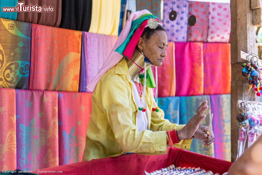 Immagine Una donna dal lungo collo vende oggetti tradizionali nel villaggio di Mae Hong Son, Thailandia. Si tratta di un'etnia della popolazione dei Karen le cui donne indossano dei cerchi di ottone che allungano il collo - © yanadhorn / Shutterstock.com