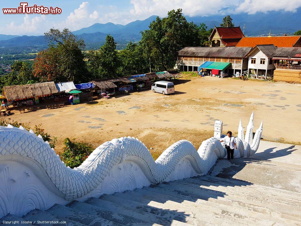 Immagine Una donna sale le scale del tempio rurale di Mae Hong Son decorato con un drago in stucco bianco, Thailandia - © icosha / Shutterstock.com