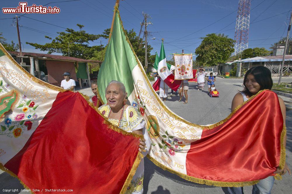 Immagine Donne camminano per le strade di Puerto Morelos con la bandiera messicana e statue religiose - © Joseph Sohm / Shutterstock.com