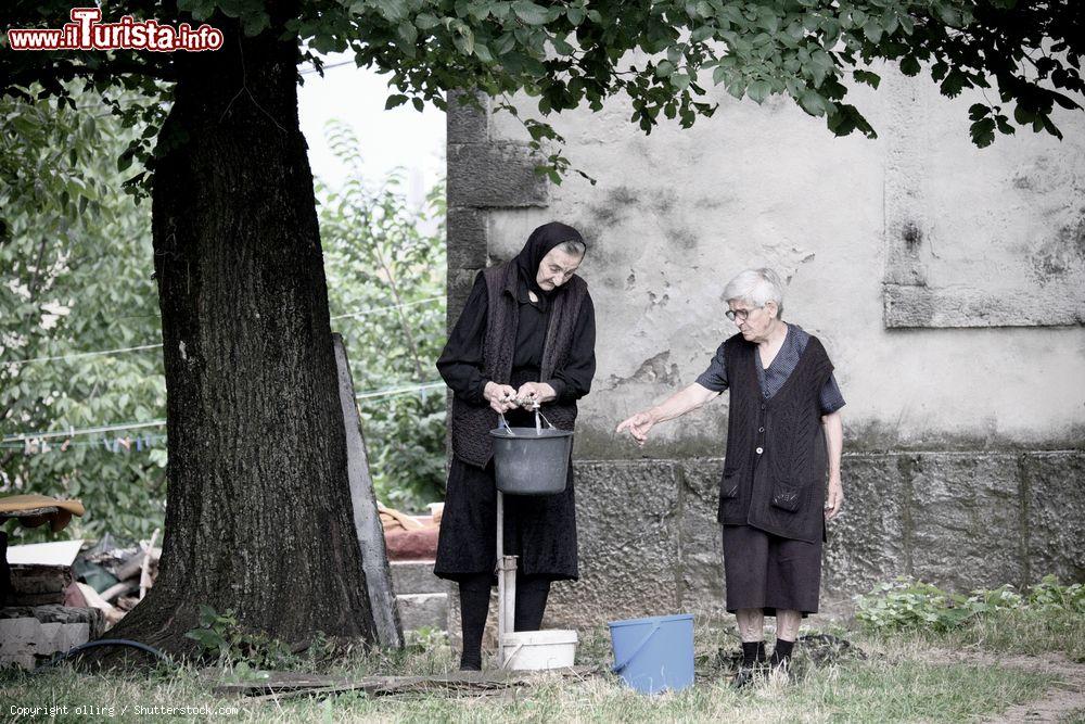 Immagine Due anziane donne con abiti neri intente a prendere acqua da una fontana a Niksic, Montenegro - © ollirg / Shutterstock.com