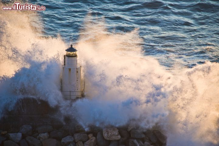 Immagine Il bianco faro di Camogli svetta nel mare in tempesta - il faro di Camogli si trova nell'estremo ovest della cittadina e la sua storia è incerta. Ciò che si sa, è che apparve nella prima metà del '900 e che fu costruito e ricostruito più volte a causa dell'usura del mare. L'ultima ricostruzione risale agli anni '70. - © Luisa Puccini / Shutterstock.com