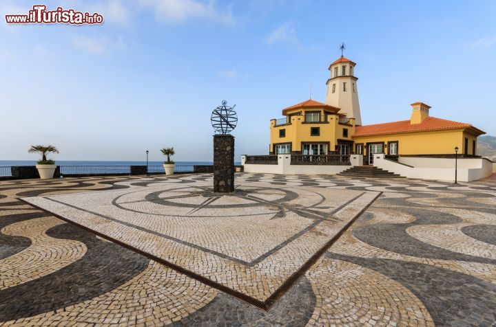 Immagine Il tipico faro dell'isola di Madeira in Portogallo - Quando si pensa al faro di una località affacciata sul mare, viene immediatamente in mente uno scenario fatto di spazi liberi affacciati nel blu. Questo a Madeira avviene, solo che come si può vedere dall'immagine ha un valore aggiunto. Questo è dato dalla bellissima piazza fatta di ciottoli che riprendono nel loro motivo geometrico la forma delle onde. Sembra infatti di fluttuare nella terra, una sensazione meravigliosa data anche dai contrasti di colore del pavimento con tinte più scure che si sposano benissimo con l'allegro giallo della struttura dove appunto, vi è collocato il faro - © Pawel Kazmierczak / Shutterstock.com