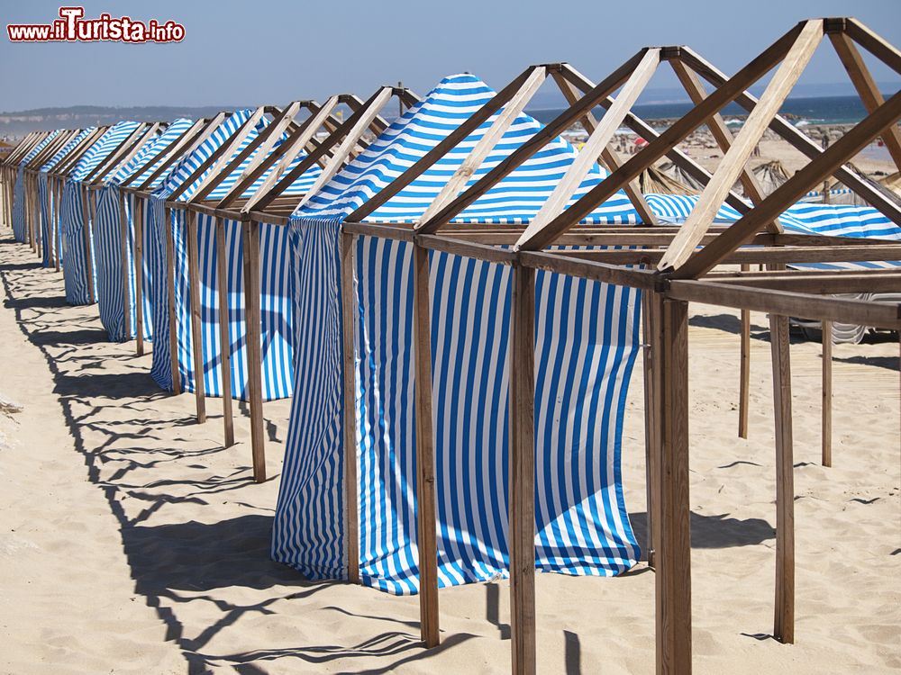 Immagine Una fila di casette con teli bianchi e blu sulla spiaggia di Costa da Caparica, Portogallo.