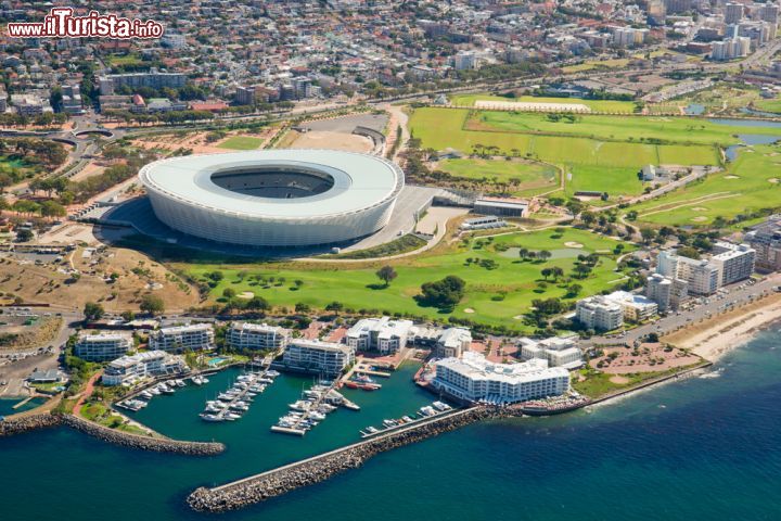Immagine Foto aerea dello Stadio di Cape Town (Sud Africa) - Cape Town Stadium o Green Point Stadium, quest'area fatta (ri)costruire nel 2010 in occasione dei mondiali di calcio, oggi rappresenta un punto importante per la collettività. Moltissimi i turisti che si lasciano affascinare dalla sua architettura oltre che dal suo significato, dall'aereo la sua presenza si percepisce benissimo e desta anche molta curiosità, vista la forma a ciambella così particolare che regna protagonista sulla località e il verde circostante - © John-james Gerber / Shutterstock.com