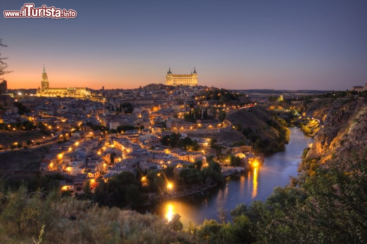Immagine Un romantico panorama di Toledo al crepuscolo, con le luci cittadine che si riflettono sulla superficie del Tago e la sagoma illuminata del Castello dell'Alcazar sullo sfondo  - © Francesco R. Iacomino / Shutterstock.com