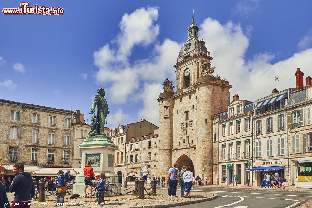 Immagine Gente a passeggio nella vecchia cittadina di La Rochelle, Francia. Sulla destra, la porta del grande orologio costruita in mattoni - © Nevskii Dmitrii / Shutterstock.com