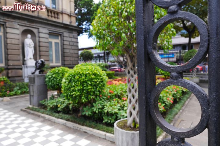 Immagine Dietro i cancelli in ferro del Teatro Nazionale di San José, Costa Rica. Un grazioso scorcio panoramico dei giardini che impreziosiscono il Teatro della capitale - © aceshot1 / Shutterstock.com