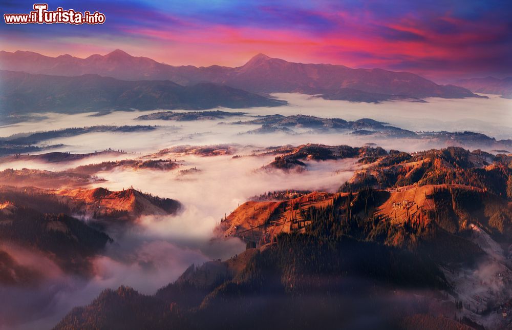 Immagine I villaggi di Vorohta, Bukovel, Yassin e il monte Chornohora visti dall'alto dei Carpazi, Ucraina: una fitta coltre di nebbia nasconde parte del paesaggio su cui risplendono le luci rossastre del tramonto.