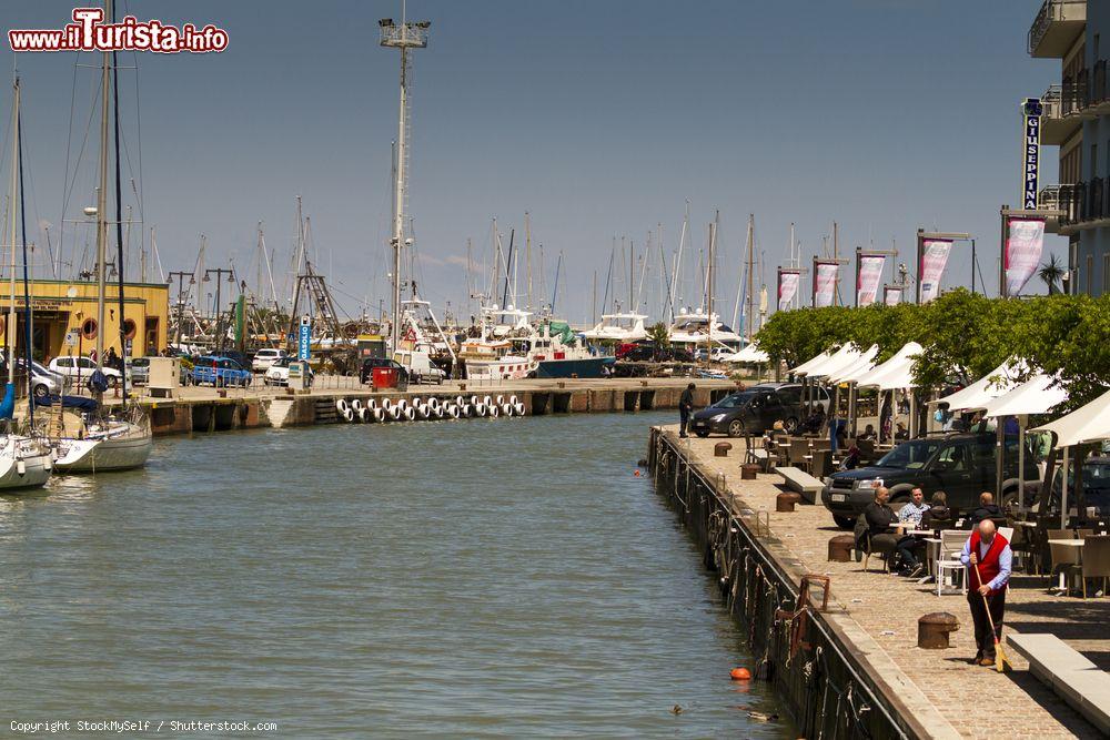Immagine Il canale di Gabicce Mare al porto, Marche. Sulla sponda destra, gente seduta ai tavolini di un caffé-ristorante - © StockMySelf / Shutterstock.com