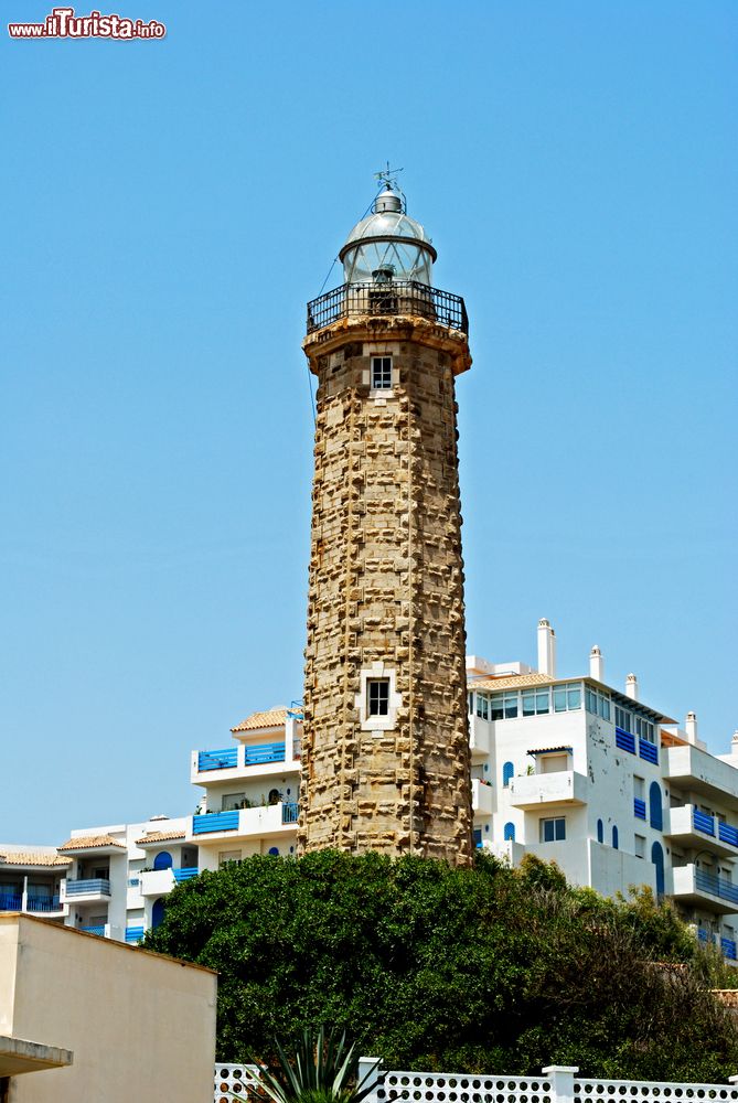 Immagine Il faro di Estepona con edifici e palazzi sullo sfondo, provincia di Malaga, Spagna. Si trova a Punta Doncella e risale agli anni '20 del 1900. Attorno ci sono giardini con aiuole e una bella varietà di alberi e arbusti.