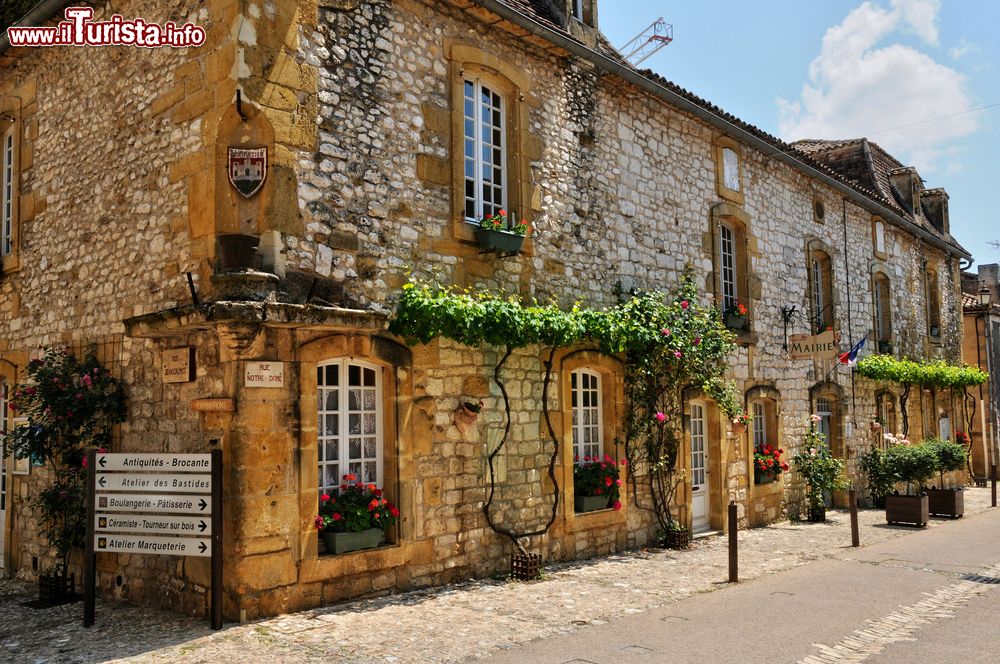 Immagine Il grazioso Palazzo Municipale di Monpazier, Francia: si tratta di un'antica costruzione in pietra abbellita da fiori colorati e piante rampicanti.