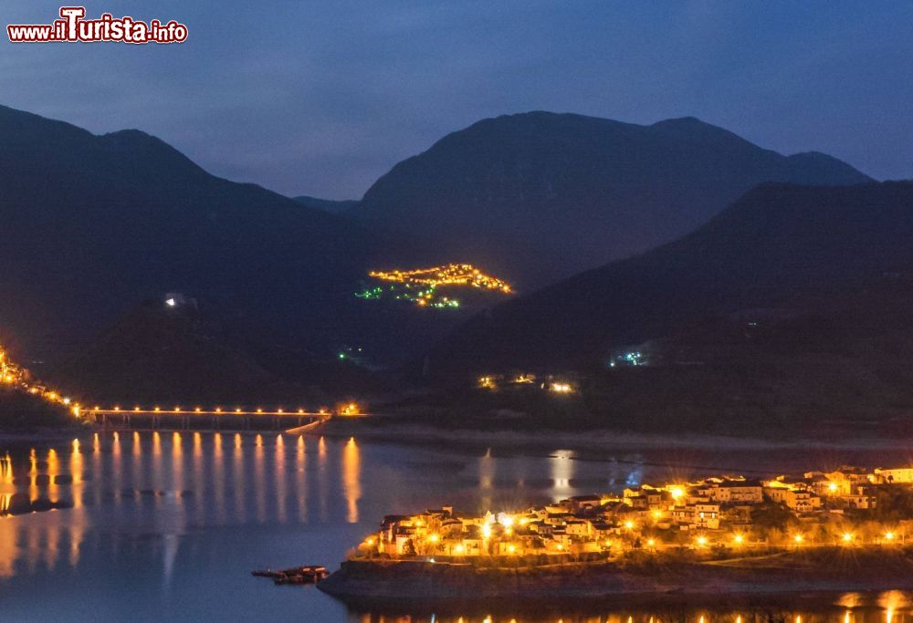 Immagine Il lago di Turano nel Lazio con le luci di Castel di Tora e, sullo sfondo, il borgo illuminato di Ascrea. Situato in provincia di Rieti, Ascrea è un centro agricolo della Sabina, nella media valle del Turano. Domina da uno sperone roccioso nei pressi del Monte Navegna al confine con la gola dell'Obito.