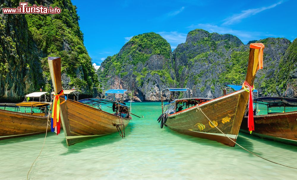 Immagine La famosa spiaggia di Maya Bay sull'isola di Phi Phi, Thailandia. In primo piano barche in legno e sullo sfondo colline calcaree con vegetazione. Sabbia bianca, acqua limpida e rocce che spuntano dal mare fanno di questo luogo una meta da sogno.