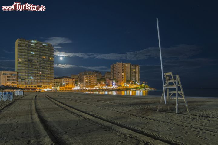 Immagine La spiaggia di Oropesa del Mar fotografata di notte, Spagna. Le luci dei palazzi che si affacciano sul lungomare si riflettono nelle acque della baia e rischiarano la fine sabbia dorata delle spiagge