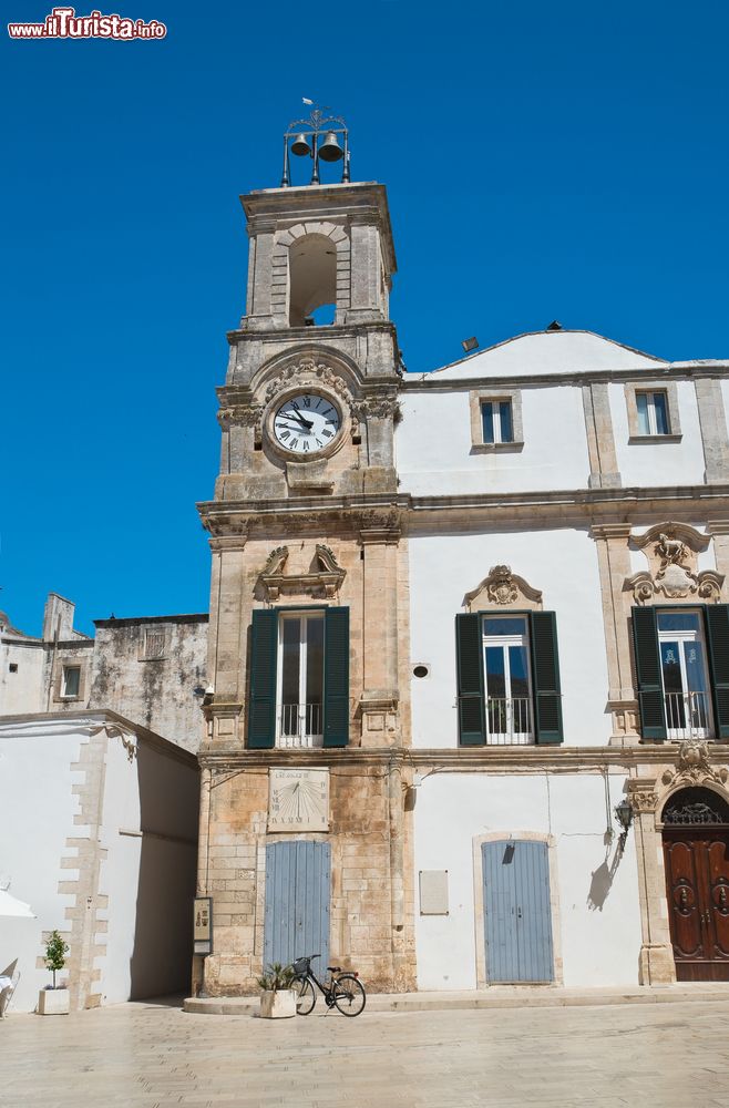 Immagine La torre dell'orologio a Martina Franca, Puglia. La slanciata torre civica della città si presenta a pianta quadrata e si eleva a quattro livelli, ognuno con caratteristiche architettoniche e decorative differenti. Realizzata in pietra locale, la torre si integra perfettamente con l'adiacente palazzo dell'Università.
