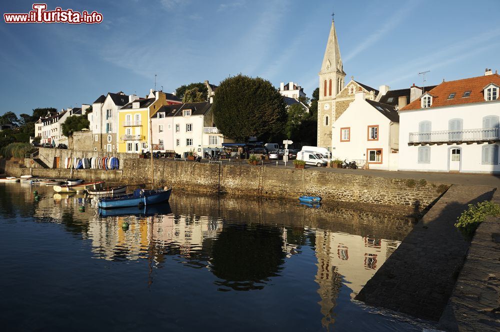 Immagine Le case e la chiesa di un villaggio di Belle Ile en Mer, Francia, riflesse nelle acque dell'Oceano Atlantico.