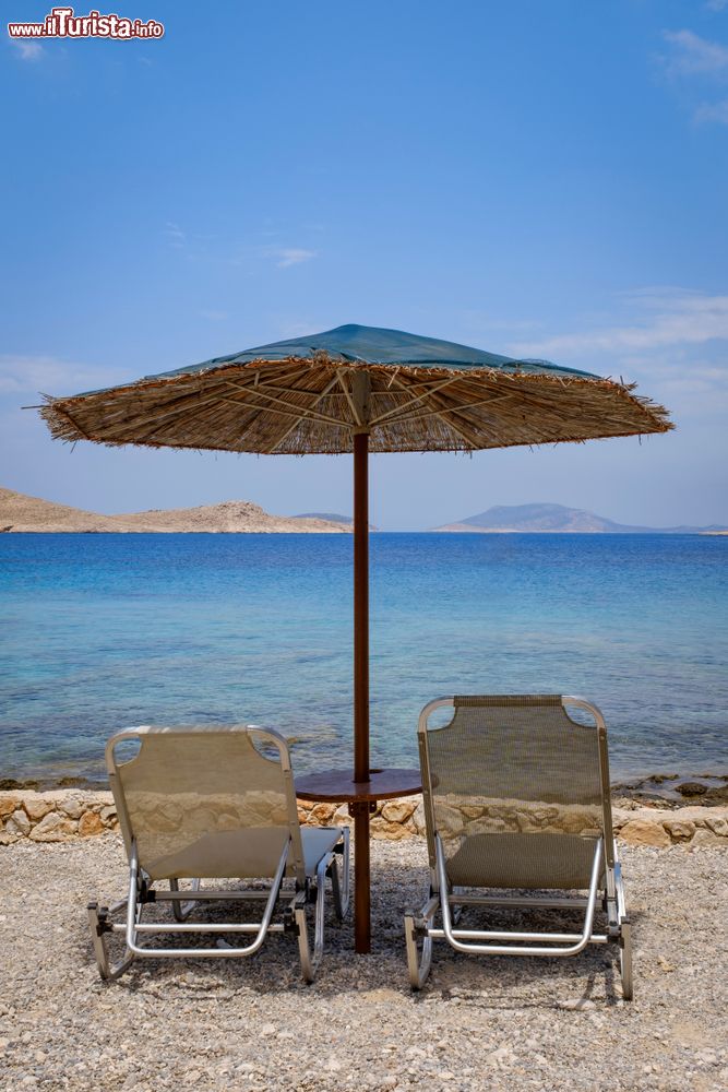 Immagine Lettini e ombrellone in paglia su una tranquilla spiaggia di Chalki, Dodecaneso, Grecia.