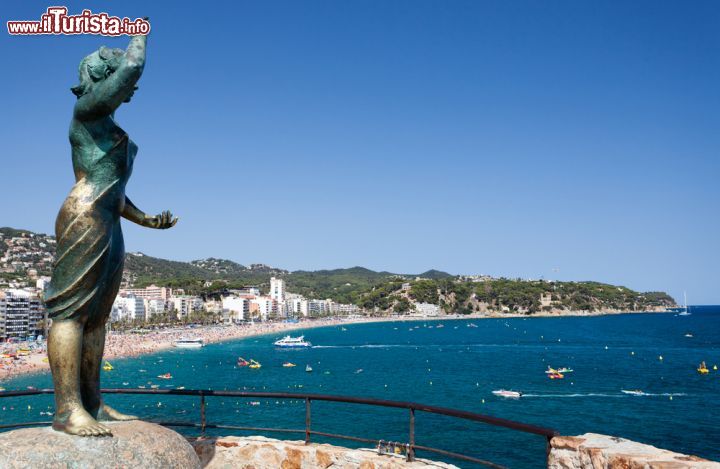 Immagine Monumento alla "moglie dei marinaio/pescatore" scultura bronzea eretta nel 1966 per commemorare il millennio a Lloret de Mar, Spagna - Che sia una delle mete turistiche più gettonate di tutta la Spagna lo si sa. Grazie infatti alla qualità delle sue acque, all'offerta gastronomica e a quella alberghiera per tutte le tasche, Lloret de Mar sa offrire una risposta adeguata alle richieste sempre più diversificate dei tanti turisti. Nonostante sia piuttosto caotica e con grandi palazzi, questa località a 60 km da Barcellona offre bei panorami così come monumenti e luoghi interessanti da visitare. In primo piano, la "Venere di Lloret" statua bronzea che ritrae una donna intenta a scrutare il mare: dal 1996, anno in cui venne inaugurata, è uno dei monumenti più fotografati della città © fototehnik / Shutterstock.com