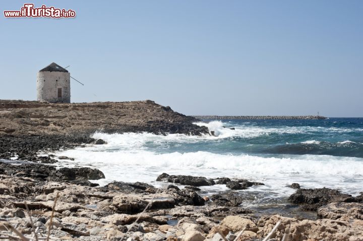 Immagine Il mulino a vento che regna sulla costa di Kassos, Dodecaneso (Grecia) - Impossibile non pensare al romanzo il cui protagonista, Don Chisciotte, sfidava i mulini a vento pur di continuare imperterrito nelle sue convinzioni. Questa porzione di costa di Kassos assume una valenza quindi per certi versi anche profonda. Le tante scogliere di cui è dotata l'isola che si trova più a sud di tutto l'arcipelago del Dodecaneso, offre moltissimi scenari come quelli visibili dall'immagine, fatto di grossi scogli dove il mare si culla e dei tratti percorribili a piedi che sfociano in un curioso mulino a vento - © Antlio / Shutterstock.com