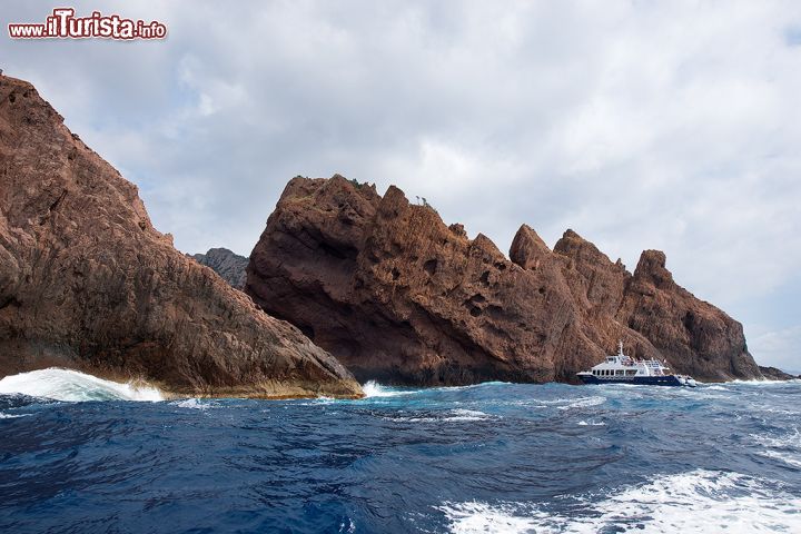 Immagine Un'imbarcazione turistica tra le scogliere di Scandola, in Corsica - le imbarcazioni che propongono la visita della bellissima Riserva naturale di Scandola partono da numerose località della costa, quali Ajaccio, Calvi, Porto e molte altre. Durante queste escursioni, a stretto contatto con la splendida natura di Scandola, è possibile avvistare specie faunistiche di straordinaria bellezza come l'aquila pescatrice, il cormorano capelluto e persino gruppi di delfini. 