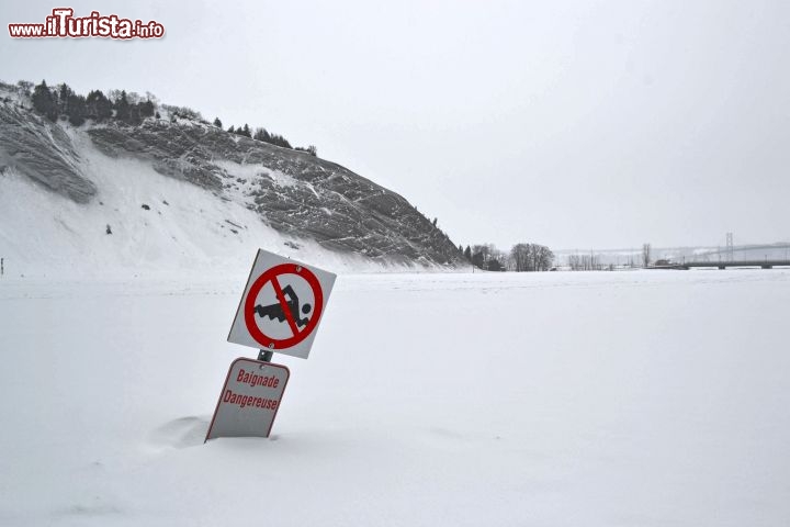 Immagine Il fiume Montmorency ghiacciato e coperto di neve in Quebec. Il cartello avverte della pericolosità del nuoto nelle acque del fiume Montmorency. In inverno le sue acque sono completamente ghiacciate e la gente vi cammina sopra per raggiungere i piedi della cascata.