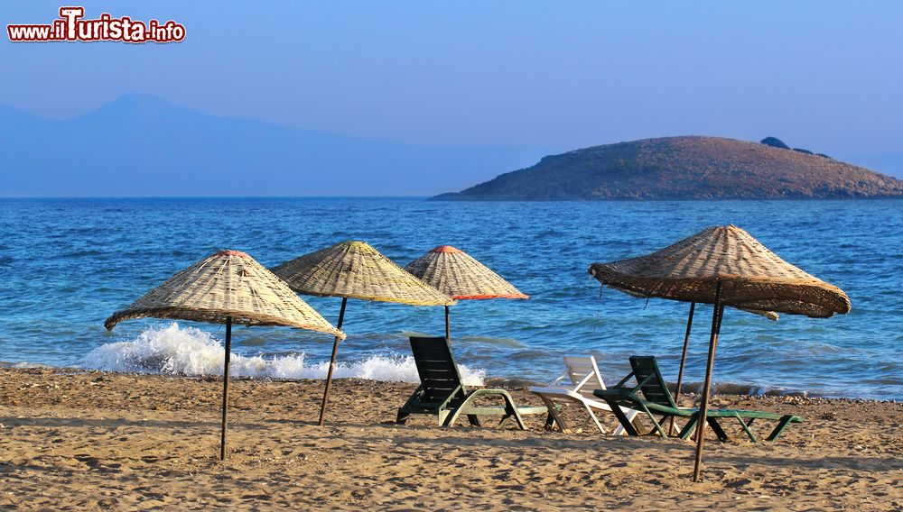 Immagine Ombrelloni in paglia e sdraio su una spiaggia di Gumuldur, Turchia. Grazie alle sue acque cristalline, alle spiagge di sabbia e ghiaia e alle numerose bellezze naturali, questa località è diventata con il tempo una delle più frequentate destinazioni vacanziere di questo tratto di costa.