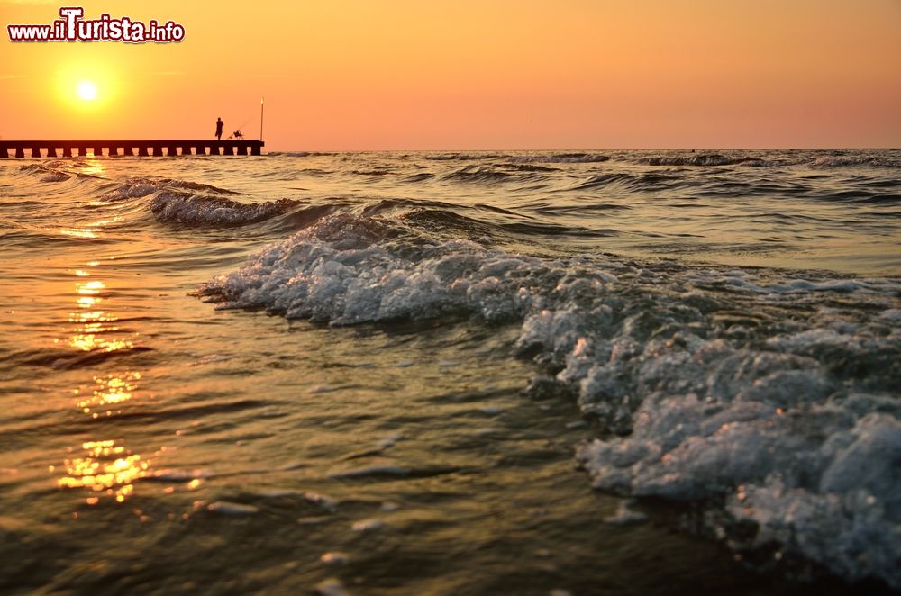 Immagine Onde del mare al tramonto sulla spiaggia di Jesolo, Veneto. Sullo sfondo, un pescatore sul pontile.