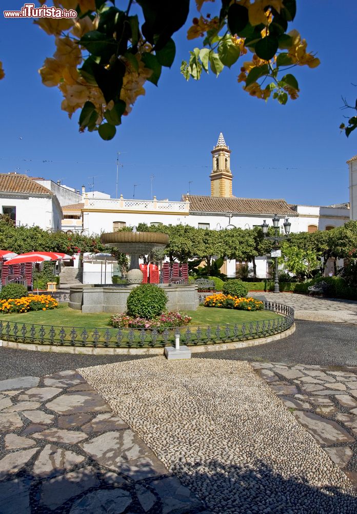 Immagine Orange Square a Estepona, Costa del Sol: la piazzetta è fotografata in una giornata di sole con prato all'inglese e fiori colorati.