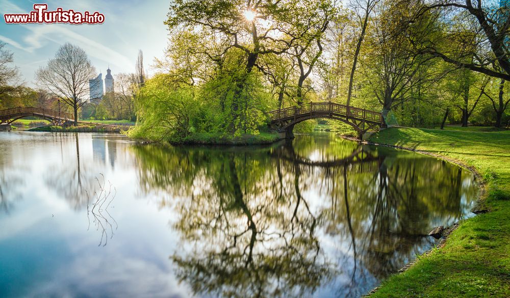 Immagine Paesaggio bucolico al Johanna Park di Lipsia, Germania, con un grazioso ponte e il lago. Sullo sfondo, la City-Hochhaus e la torre del Municipio.