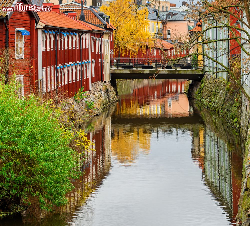 Immagine Paesaggio naturale con le tipiche case in legno e un ponte sullo sfondo, Vasteras, Svezia. I colori dell'autunno si riflettono nelle acque di questo canale.