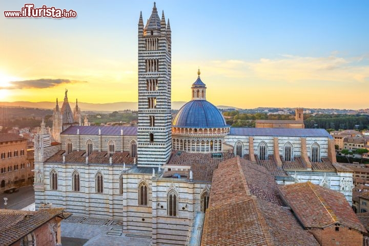 Immagine Il Duomo di Siena al tramonto. Fu realizzato come residenza del Vescovo a partire dalla seconda metà del XII secolo su un preesistente edificio, e venne convertito in Basilica solo il secolo successivo. Il campanile, alto circa 77 m, fu invece completato nel 1313. La luce della sera valorizza la facciata in marmo bianco con dettagli rosa - © StevanZZ / Shutterstock.com