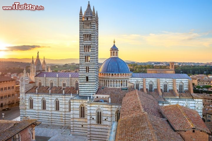 Immagine Il Duomo di Siena al tramonto. Fu realizzato come residenza del Vescovo a partire dalla seconda metà del XII secolo su un preesistente edificio, e venne convertito in Basilica solo il secolo successivo. Il campanile, alto circa 77 m, fu invece completato nel 1313. La luce della sera valorizza la facciata in marmo bianco con dettagli rosa - © StevanZZ / Shutterstock.com