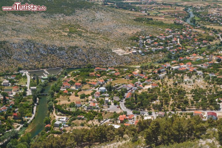 Immagine Blagaj dall'alto: la città monumento della Bosnia-Erzegovina tra colline e pianure - una splendida veduta panoramica di Blagaj e della pianura di  Bišće, nel profondo sud della Bosnia-Erzegovina. Il villaggio di Blagaj è situato a pochi chilometri dalla famosa Mostar, ed è considerato uno dei massimi patrimoni naturlastici e architettonici della nazione, grazie soprattutto al tempio derviscio, costruito proprio di fianco a una bellissima sorgente.  - © Lev Levin / Shutterstock.com