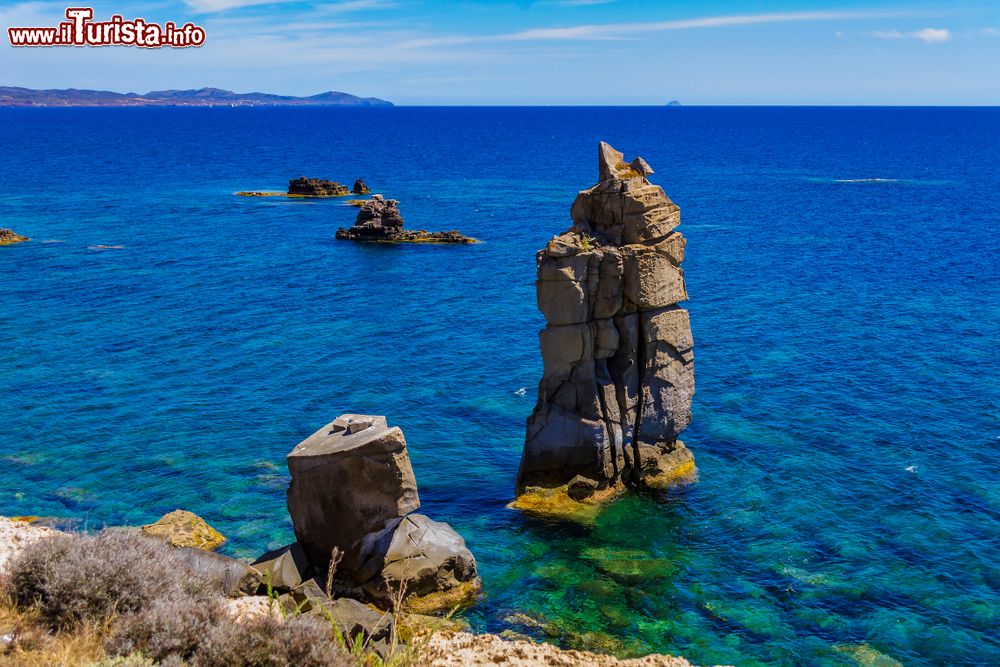 Immagine Panorama delle rocce vulcaniche note come Le Colonne a Carloforte, isola di San Pietro, Sardegna. Dal mare blu s'innalzano due pilastri naturali di colore grigio scuro in uno scenario fatto di calette, promontori e falesie.