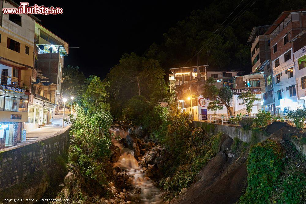 Immagine Panorama notturno di Aguas Calientes, Perù. Uno scorcio del celebre villaggio nei pressi di Machu Picchu con le sue costruzioni affacciate sulle viuzze strette e con al centro la cascata sul fiume Urubamba - © PixieMe / Shutterstock.com