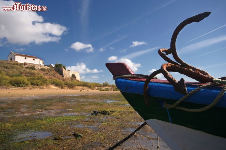 Immagine Particolare di un'imbarcazione a Cacela Velha, Portogallo - Il dettaglio di una tipica barca da pesca con la chiesa e la fortezza di Cacela Velha sullo sfondo. I panorami che si possono ammirare in questo angolo di Algarve sono fra i più suggestivi di tutto il Portogallo © AMA / Shutterstock.com