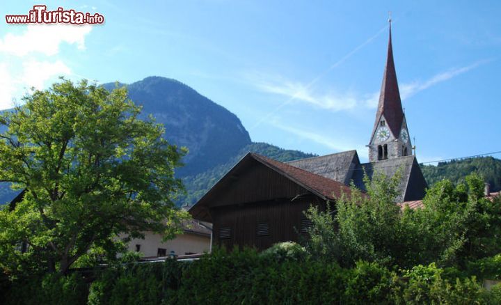 Immagine Il campanile della chiesa svetta tra i tetti di Jenbach, Austria - la Pfarrkirche (chiesa parrocchiale) dedicata ai Santi Wolfgang e Leonhard, svetta tra i tetti di Jenbach con il suo bellissimo campanile in pietra. Sullo sfondo, le splendide montagne del Tirolo austriaco, tra cui spicca il massiccio del Karwendel.