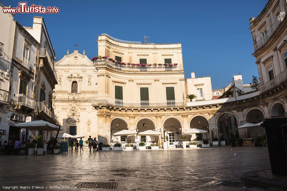 Immagine Piazza Santa Maria Immacolata a Martina Franca con bar e turisti, Puglia. Chiamata comunemente "I Portici", questa piazza è il salotto elegante della città pugliese. Oggi ospita eventi e manifestazioni di ogni genere oltre ad essere il luogo ideale per gustare le specialità gastronomiche di Martina Franca - © Angelo D'Amico / Shutterstock.com