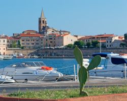 La Baia di Alghero in provincia di Sassari, Sardegna: il porto turistico che collega la città alle Grotte di Nettuno, il lungomare, le prime case e il campanile della Cattedrale di Santa ...