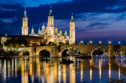 Il centro storico di Saragozza visto dal fiume Ebro e la Cattedrale illuminata. Di notte, con le luci delle strade e dei palazzi che si riflettono sull'acqua, la città araba e europea ...