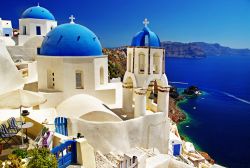 Le chiese di Santorini, con le paricolari cupole blu, sullo sfondo la caldera del Vulcano Neo Kameni: siamo nell'arcipelago delle Cicladi in Grecia - © leoks / Shutterstock.com